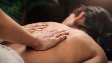Person lying face down receiving a back massage as a therapist's hands press and glide across their upper back