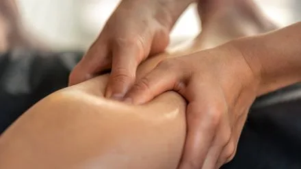 Two hands pressing and kneading a person's calf in a close-up massage