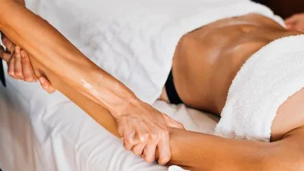 Person reclined on a massage table, covered by a towel, receiving an oiled arm and shoulder massage from therapist's hands.