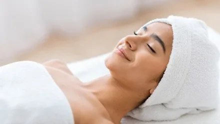Relaxed woman with a towel wrapped around her hair and shoulders, lying back with eyes closed and a slight smile during a spa treatment.